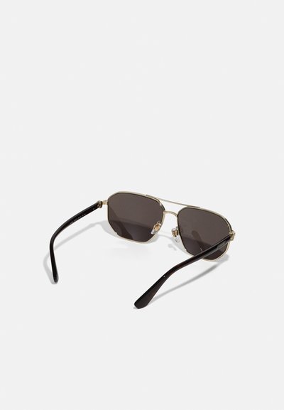 Óculos de sol com armação metálica dourada e lentes escurecidas em cinza escuro, de forma octagonal, com braços do templo em plástico preto. Almofadas de nariz notáveis para conforto.