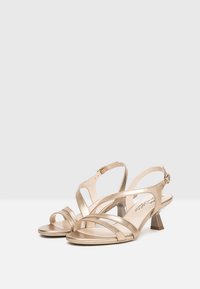 Gold metallic high-heeled sandals with open toes, featuring crisscross straps and an adjustable ankle buckle. Textured finish and block heel.