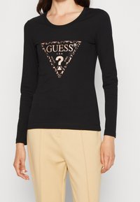 Schwarz langärmliges T-Shirt mit einem dreieckigen Leopardenprint-Logo und metallischen Akzenten. Der Stoff ist glatt und dehnbar.