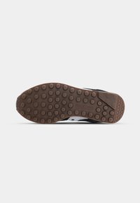 Black sneaker with a textured fabric upper, white accents, and a brown rubber sole featuring circular grip patterns.