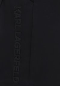 Vêtement noir arborant le logo "KARL LAGERFELD" en relief sur un côté. Texture lisse avec un design moderne et minimaliste.