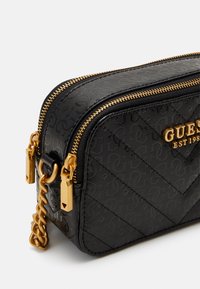 Borsa a tracolla in faux leather nera con motivo a zigzag, hardware dorato, doppia cerniera e dettaglio del logo sul fronte. Inclusa una catena decorativa.