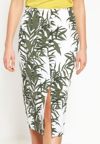 Vit kjol med grönt bladmönster, med en framklippning. Tillverkad av ett mjukt tyg, har den en figurnära design som når mitt på vadbenet.