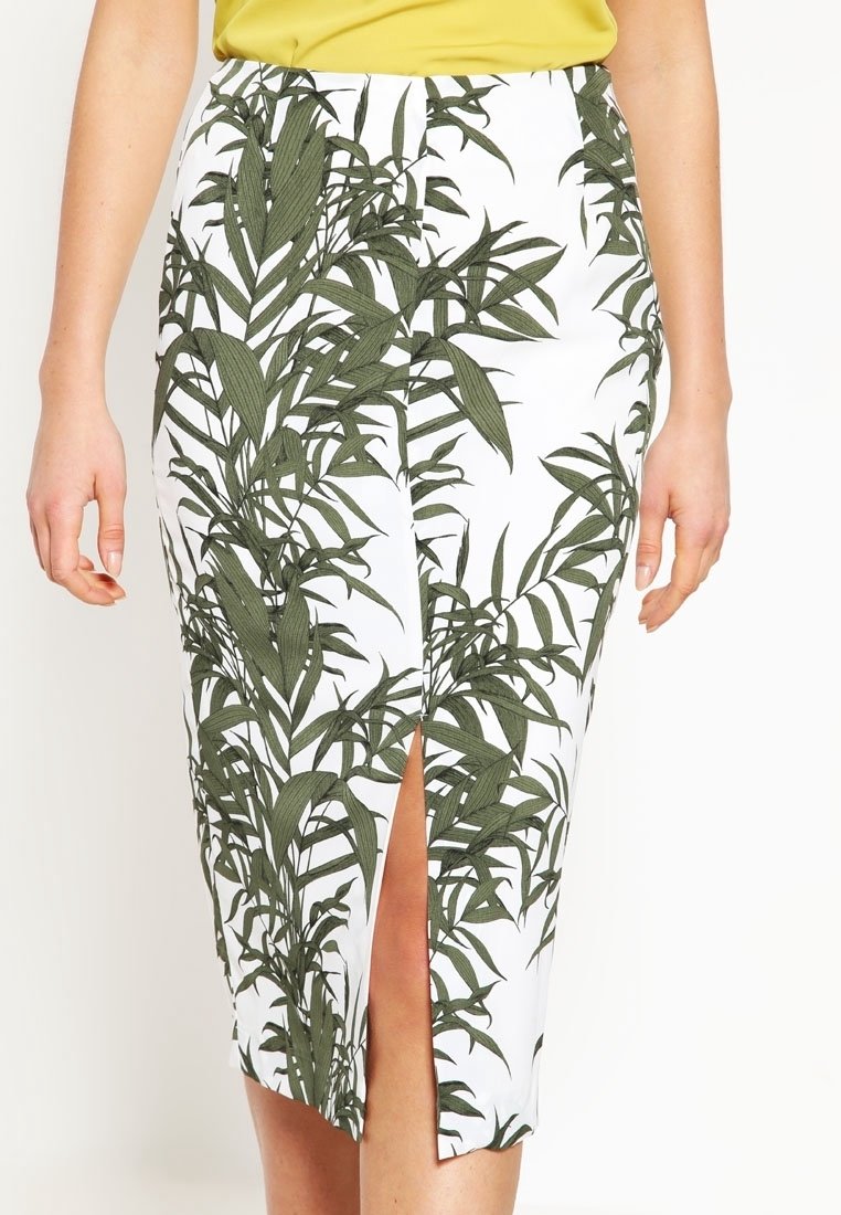 Vit kjol med grönt bladmönster, med en framklippning. Tillverkad av ett mjukt tyg, har den en figurnära design som når mitt på vadbenet.