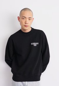 Black crew-neck sweatshirt made of soft fabric. Features a small white "Carhartt WIP" logo on the chest. Loose fit with ribbed cuffs.