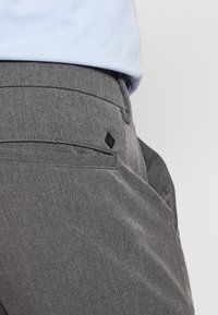 Gray trousers with a smooth texture, featuring a back pocket and a small black logo tag. Design includes subtle stitching details.