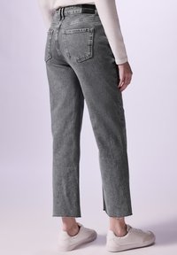 Jean en denim gris avec une coupe droite, dotés de poches arrière et d'ourlets brut, associés à des baskets blanches. Le tissu semble légèrement texturé.