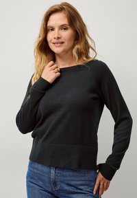 Schwarzer Strickpullover mit Rundhalsausschnitt, langen Ärmeln und gerippten Bündchen. Kombiniert mit blauen Jeans. Glatte Textur mit figurbetontem Design.