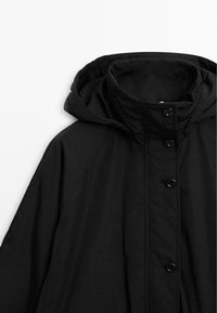 Veste noire avec capuche. Fabriquée en matière texturée, dotée d'une fermeture avant à boutons et d'un ourlet courbé. Design simple et léger.