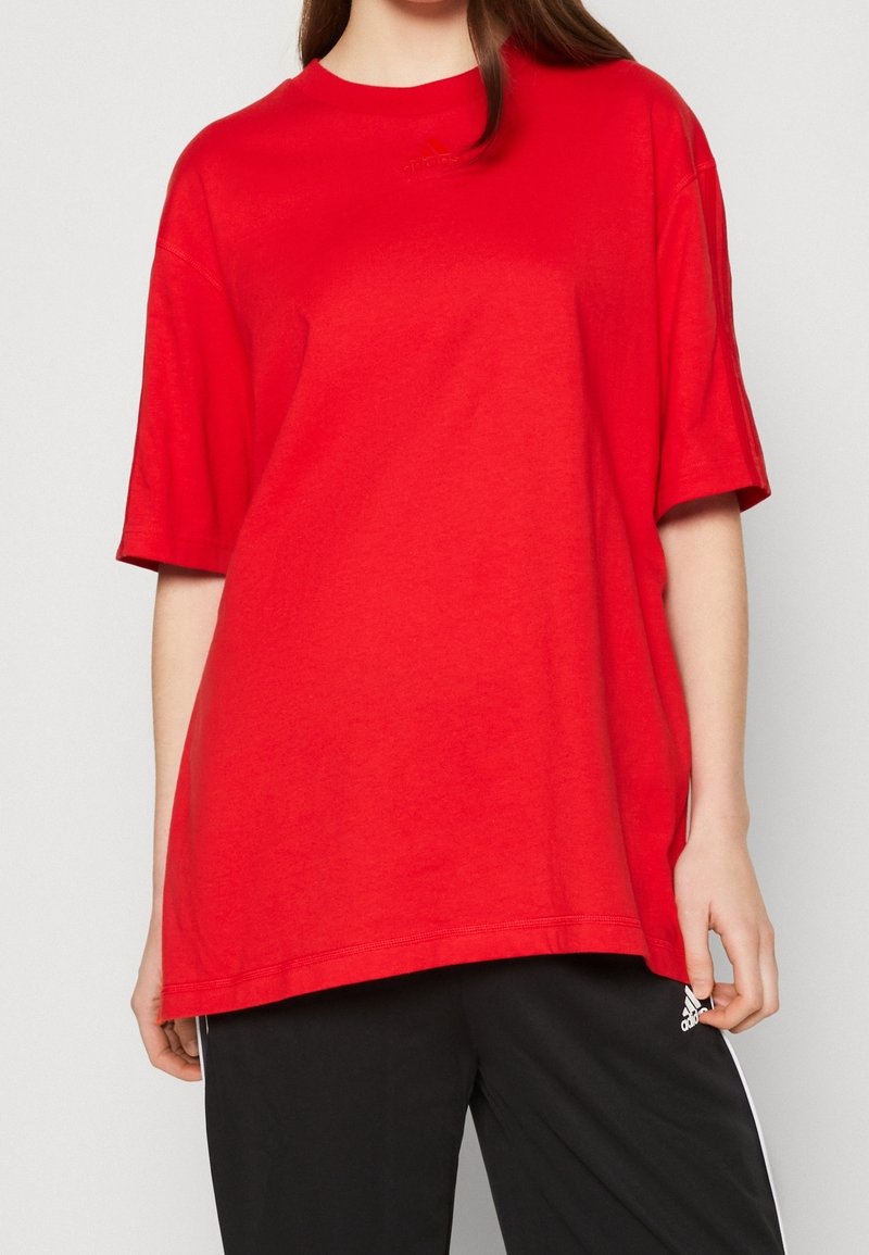 Červené bavlněné tričko s kulatým výstřihem a krátkými rukávy. Má jednoduchý design, mírně oversize střih a subtilní logo Adidas.