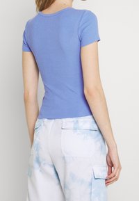 Ribbed short-sleeve top in light blue, fitted design, soft texture. Paired with high-waisted cargo pants featuring a light blue tie-dye pattern.