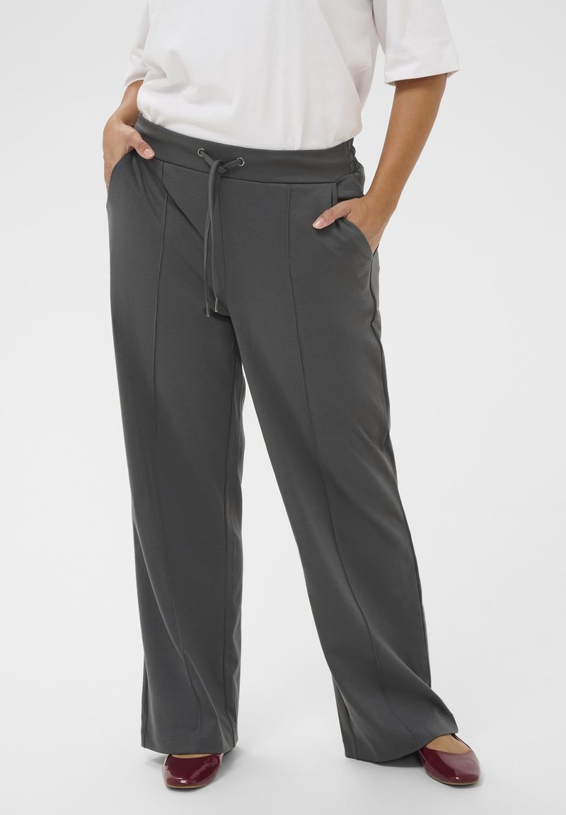 Personne portant un pantalon ample gris foncé à cordon avec poches latérales, associé à des chaussures plates rouges et un haut blanc à manches courtes.