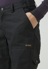Melnas G-1000 auduma bikses ar klasisku fasonu, kas ietver priekšējos kabatas un redzamu logotipu, gludu tekstūru un izturīgu konstrukciju.