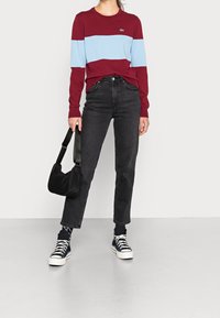 Košile s dlouhým rukávem v maroon a světle modrých pruzích, černé lační džíny, černá crossbody taška, černobílé tenisky a vzorované ponožky.