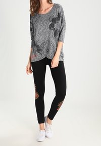 Šedý krátký rukáv top s květinovým vzorem; v kombinaci s černými legínami s akcenty květinové výšivky; bílá tenisky dokončují outfit.