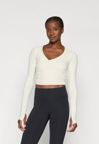Lange mouwen, crèmekleurige crop top met een V-hals en gathered details, gecombineerd met hoge zwarte leggings. Zachte stof en aansluitend ontwerp.