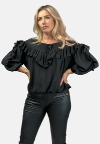 Czarna bluzka z falbaniastym dekoltem i bufiastymi rękawami. Wykonana z gładkiego materiału, posiada wiązanie przy dekolcie oraz elastyczny dół.