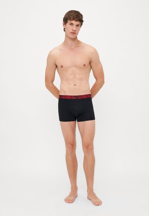 Boxer shorts noirs en tissu extensible avec une taille élastique rouge arborant un logo. Le design est simple et ajusté.