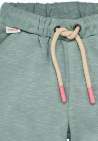 Pantaloni della tuta verde menta con finitura texturizzata, dotati di chiusura con cordino in crema e aglette rosa, e un'etichetta "BONDI".