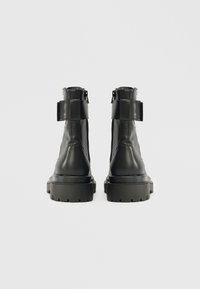 Botine negre din piele cu un upper texturat, talpă din cauciuc rezistentă și fermoare laterale. Prezintă un accent cu cataramă în spate.