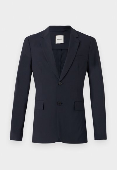 Tumeda sinine ülikonna jakk, millel on lame krae, kaks nuppu ja kaks eesmist taskut. Valmistatud siledast kangast ning sobib kehakujuga. Sildiga näha seest.