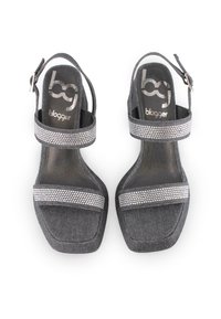 Dos sandalias de tacón alto de mezclilla negra con adornos de rhinestones plateados, diseño de punta abierta, tira para el tobillo y forma cuadrada. Textura suave.
