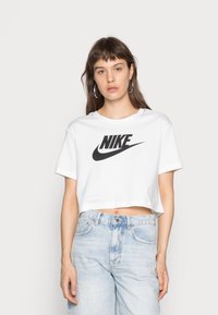 Camiseta blanca recortada con el logo negro de "Nike". Mangas cortas, cuello redondo y material de algodón suave. Combinada con jeans de mezclilla azul claro.