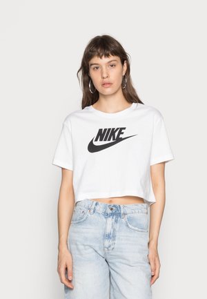 Camiseta blanca recortada con el logo negro de "Nike". Mangas cortas, cuello redondo y material de algodón suave. Combinada con jeans de mezclilla azul claro.