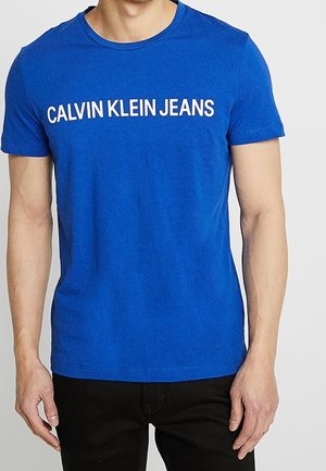 Blauwe katoenen T-shirt met witte "CALVIN KLEIN JEANS" tekst over de borst, ronde halslijn en korte mouwen.