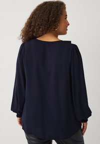 Marineblauwe blouse met lange mouwen, met geplooide schouders, een ronde halslijn en een losse pasvorm. De stof lijkt glad met een lichte glans.