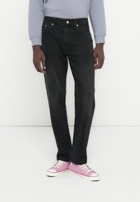 Μαύρα τζιν από denim με ίσια γραμμή, σχέδιο με πέντε τσέπες και ασημένια κουμπιά. Συνδυασμένα με ροζ αθλητικά παπούτσια για αντίθεση.