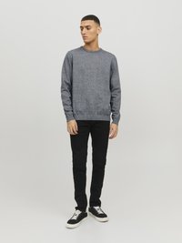 Grijze trui van textiel met structuur, ronde halslijn, gecombineerd met slim fit zwarte broeken en zwarte sneakers met witte veters.