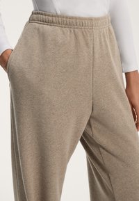 Beige collegehousut pehmeästä kankaasta, jossa on joustava vyötärönauha ja sivutaskut, rento istuvuus ja sileä pinta.