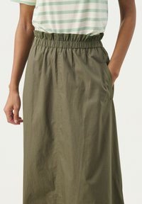 Gonna verde oliva con cintura elastica, texture uniforme e tasche laterali, abbinata a una maglietta a righe verde chiaro e bianca.