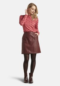 Rode gestreepte top met lange mouwen, gecombineerd met een kastanjebruine nepleer rok met twee voorkeurszakken. Draagt zwarte maillots en glanzende enkellaarsjes.