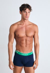 Ναυτικό μπλε μποξεράκια Lacoste με πράσινη επώνυμη ζώνη, κ�ατασκευασμένα από μαλακό ύφασμα. Εφαρμοστή σχεδίαση, που δείχνει απαλό υλικό.