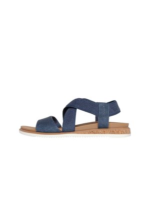 Open-toe sandal with navy blue crisscross fabric straps, tan footbed, cork midsole, and white rubber outsole.