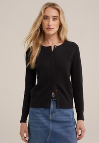 Zwarte gebreide cardigan met een ronde hals, voorzien van een textuurpatroon en sluiting met knopen, gecombineerd met een spijkerrok.