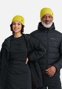 Felgekleurde gele geribbelde muts op twee personen die zwarte pufferjacks dragen. De ene heeft een capuchon, en de andere draagt een zwarte aansluitende top en rok.