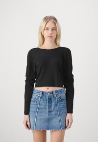 Schwarzes, geripptes Langarm-Crop-Top kombiniert mit einem hochtaillierten Denim-Rock mit fransigem Saum und kontrastierenden Nähten.