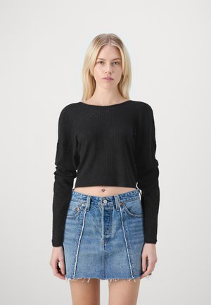 Must mustriba mustriidi pikad varrukad crop top, mis on sobitatud kõrge vöökohaga teksaseelikuga, millel on kulunud serv ja kontrastsed õmblused.