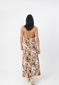 Robe maxi avec un motif floral dans des teintes terreuses, design sans dos, bretelles ajustables et tissu fluide qui atteint les chevilles.