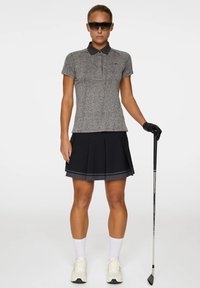 Grijs polo-shirt met korte mouwen en een zwarte kraag, gecombineerd met een geplooide zwarte rok met grijze accenten. Witte sokken en lichte schoenen.