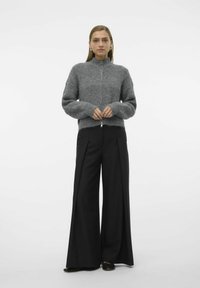 Grå strikket zip-up genser med høy krage, brede ermer og ribbestrikket tekstur, sammen med svarte vide bukser.