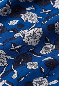Tissu bleu avec un motif floral en blanc et marine foncé, présentant diverses fleurs et feuilles, texture lisse.