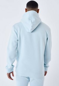 Felpa leggera blu chiaro con un grande cappuccio, realizzata in tessuto morbido. Caratterizzata da maniche lunghe e polsini a coste, progettata per comfort e calore.