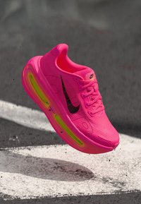 Baskets Nike rose vif avec un Swoosh noir, tige en mesh texturé, accents jaune vif et amorti à air visible dans la semelle.