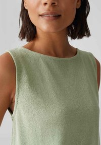 Top senza maniche verde chiaro realizzato in tessuto a maglia testurizzata, con scollatura rotonda e bordi grezzi attorno alle aperture delle maniche.