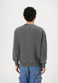 Felpa grigia scura con una vestibilità rilassata, colletto e polsini a coste, e dettagli cuciti in evidenza. Abbinata a pantaloni cargo blu.