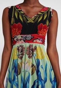 Robe fleurie avec un corsage noir agrémenté d'accents rouges et verts. La jupe évasée présente un grand imprimé floral aux couleurs pastel.